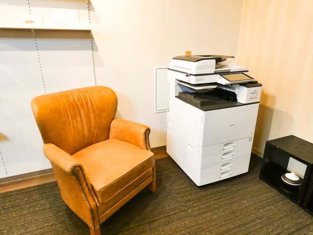 複合機_複合機の隣には様々なビジネス書が置かれた本棚とゆったりくつろげるソファーが設置されています